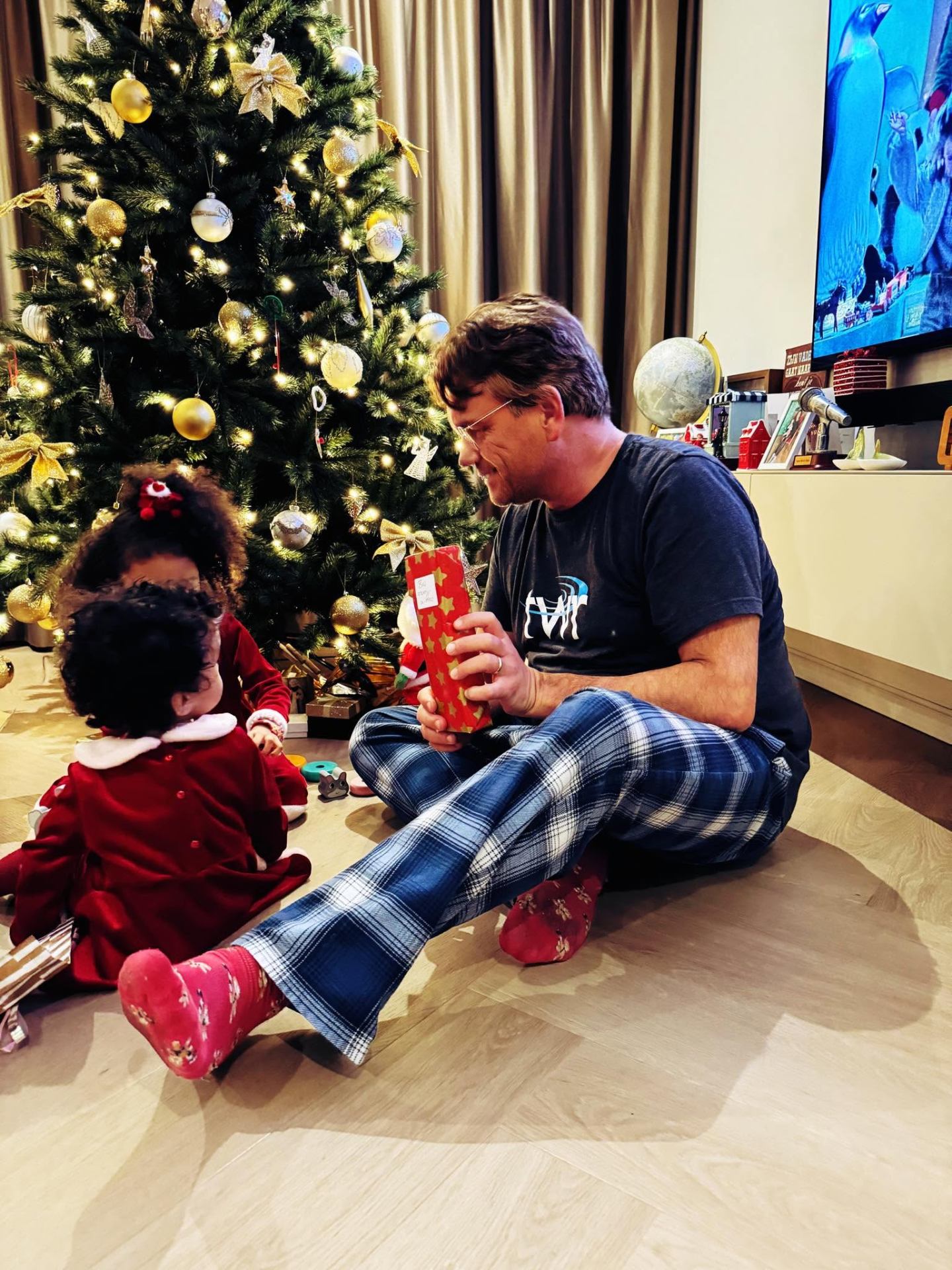 Bas geeft een cadeau bij de kerstboom aan zijn dochter — warmte, thuis, herinnering.