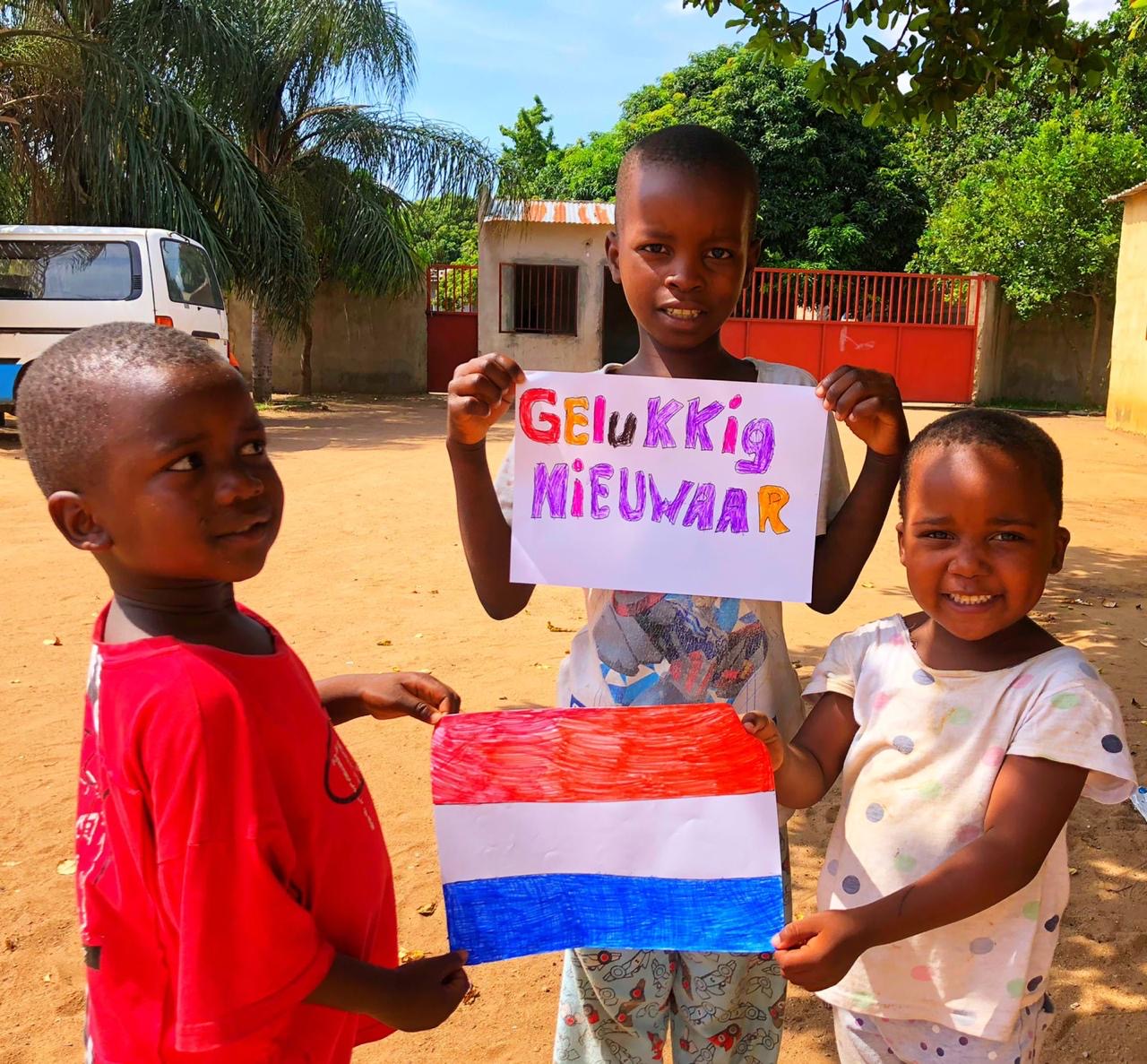Swazi kinderen houden een handgetekende Nederlandse vlag en de tekst Gelukkig Nieuwjaar omhoog
